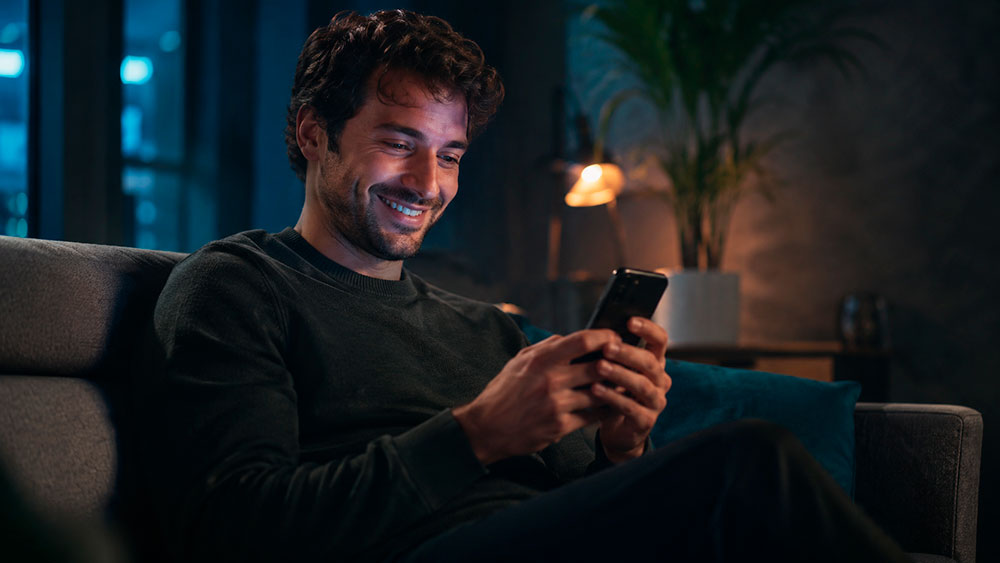Paciente no sofá de casa, à noite, enviando mensagem pelo celular